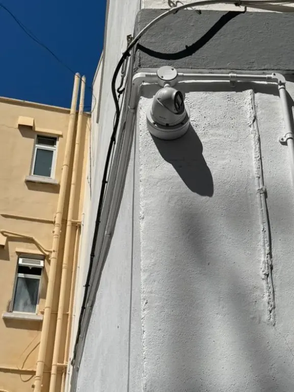 Dome camera mounted at high level on a rendered wall covering a rear lane in Gibraltar