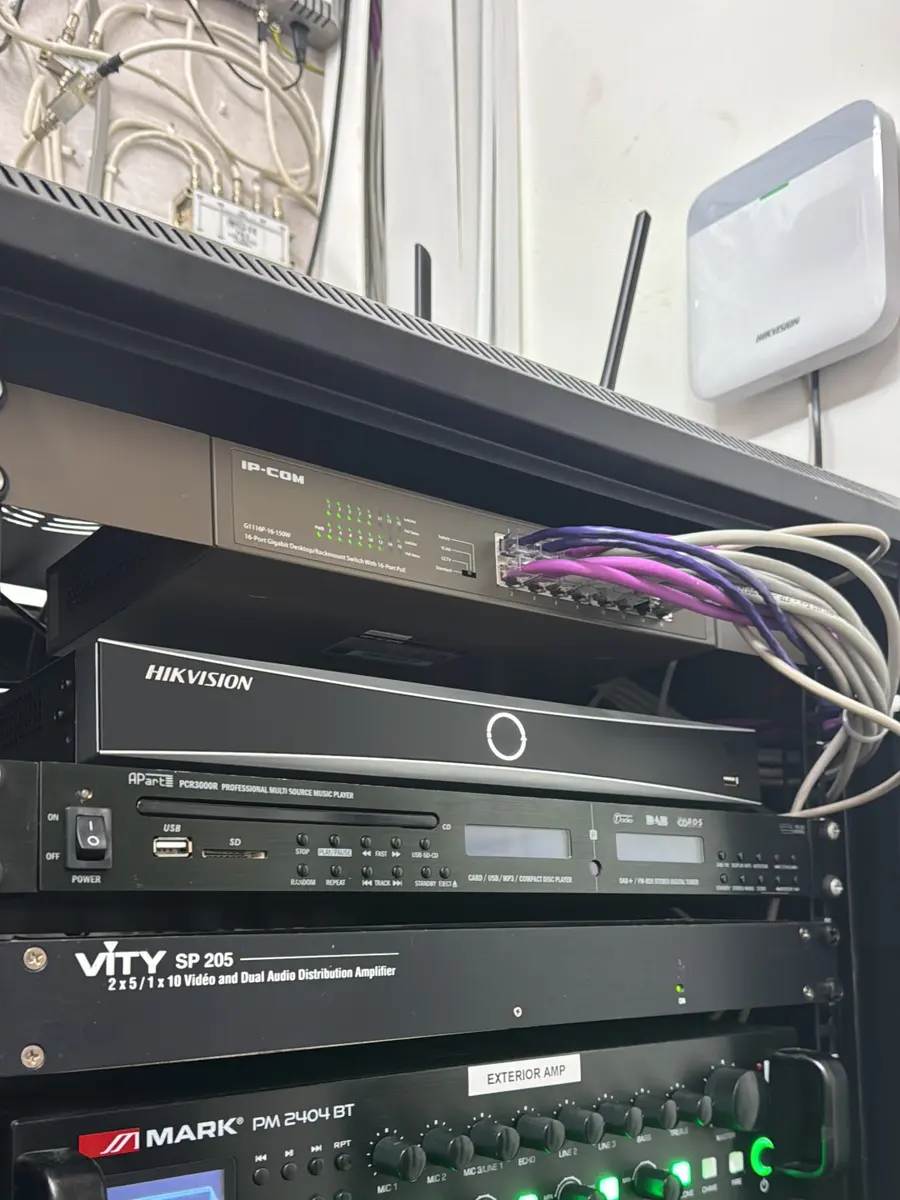 Comms rack containing a Hikvision NVR, a 16-port PoE switch and audio equipment